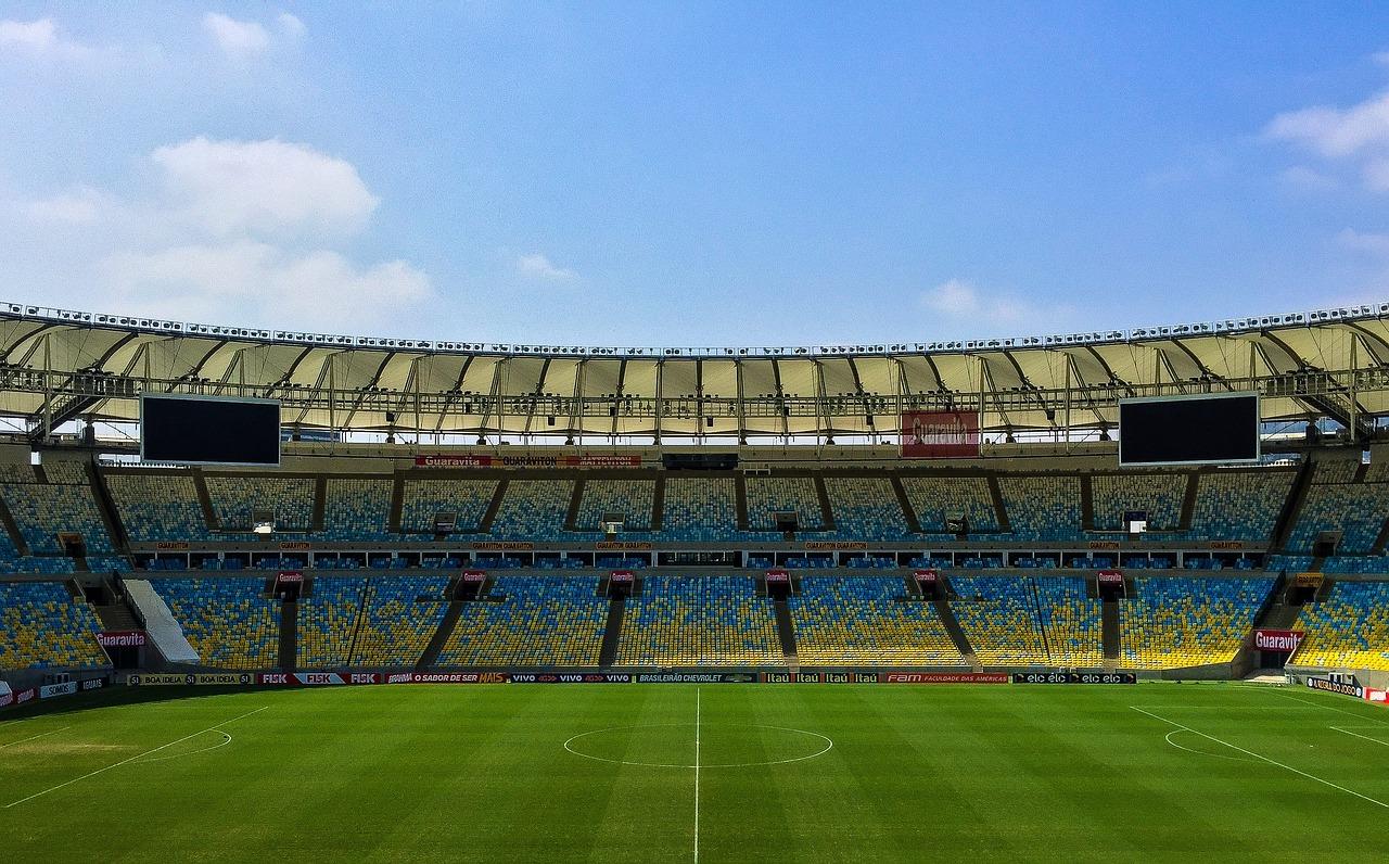 A stadium with a green field and blue seats<br><br>Description automatically generated