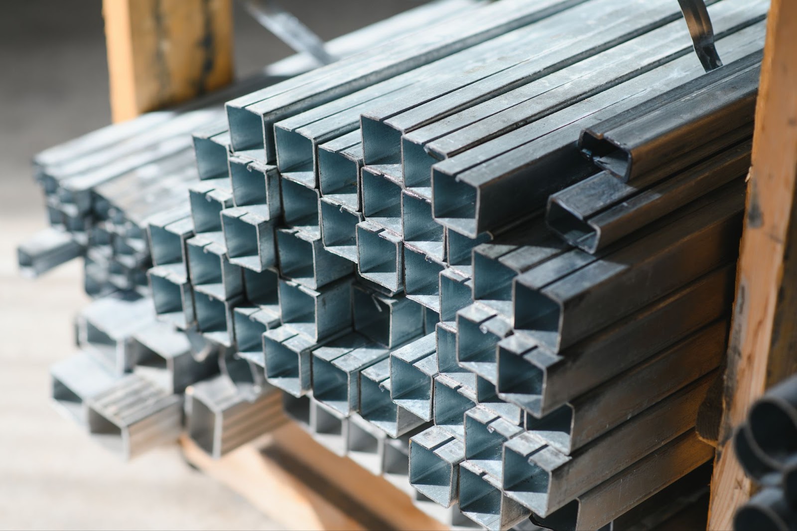 A neatly stacked pile of square galvanized steel pipes, ready for use in fence construction, displaying a metallic silver finish characteristic of galvanized steel.