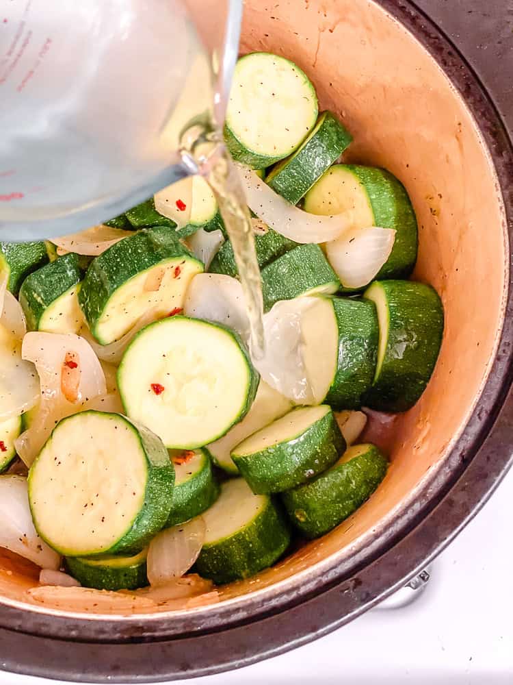 pouring water into a pot with sliced zucchini.