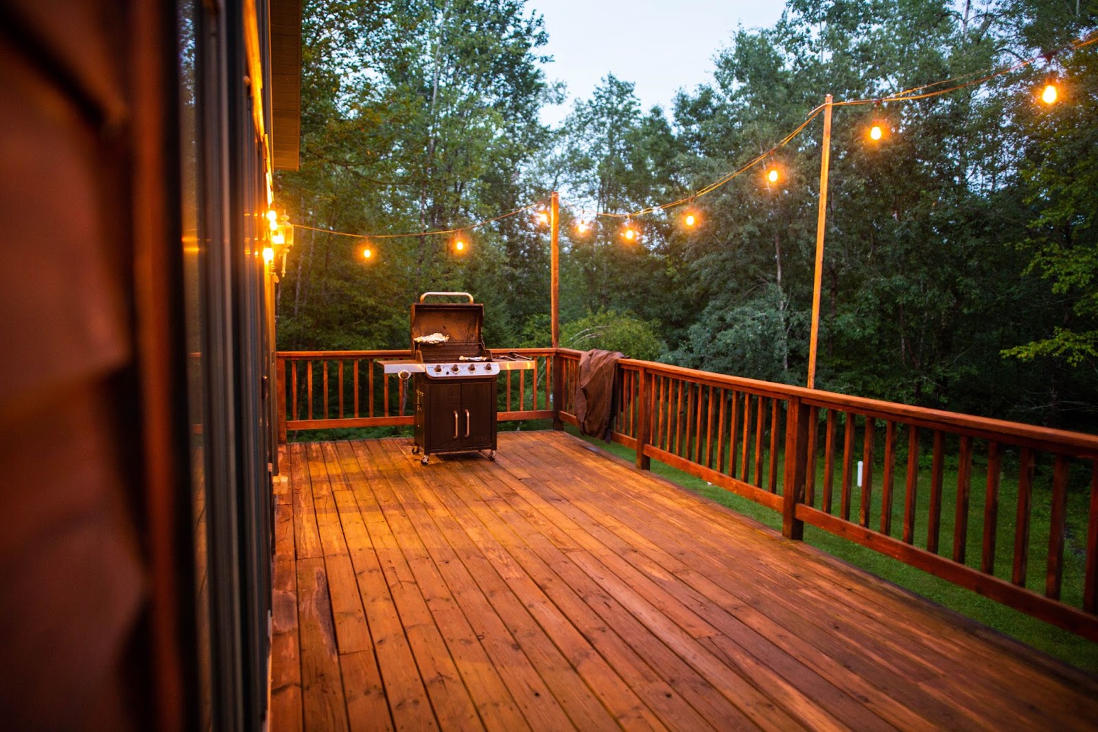 A wooden porch with string lights and a grill. 
