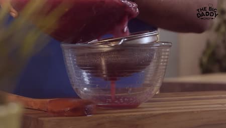 Falsa mixture being poured through a fine-mesh strainer into a bowl to separate the juice from the pulp and seeds.