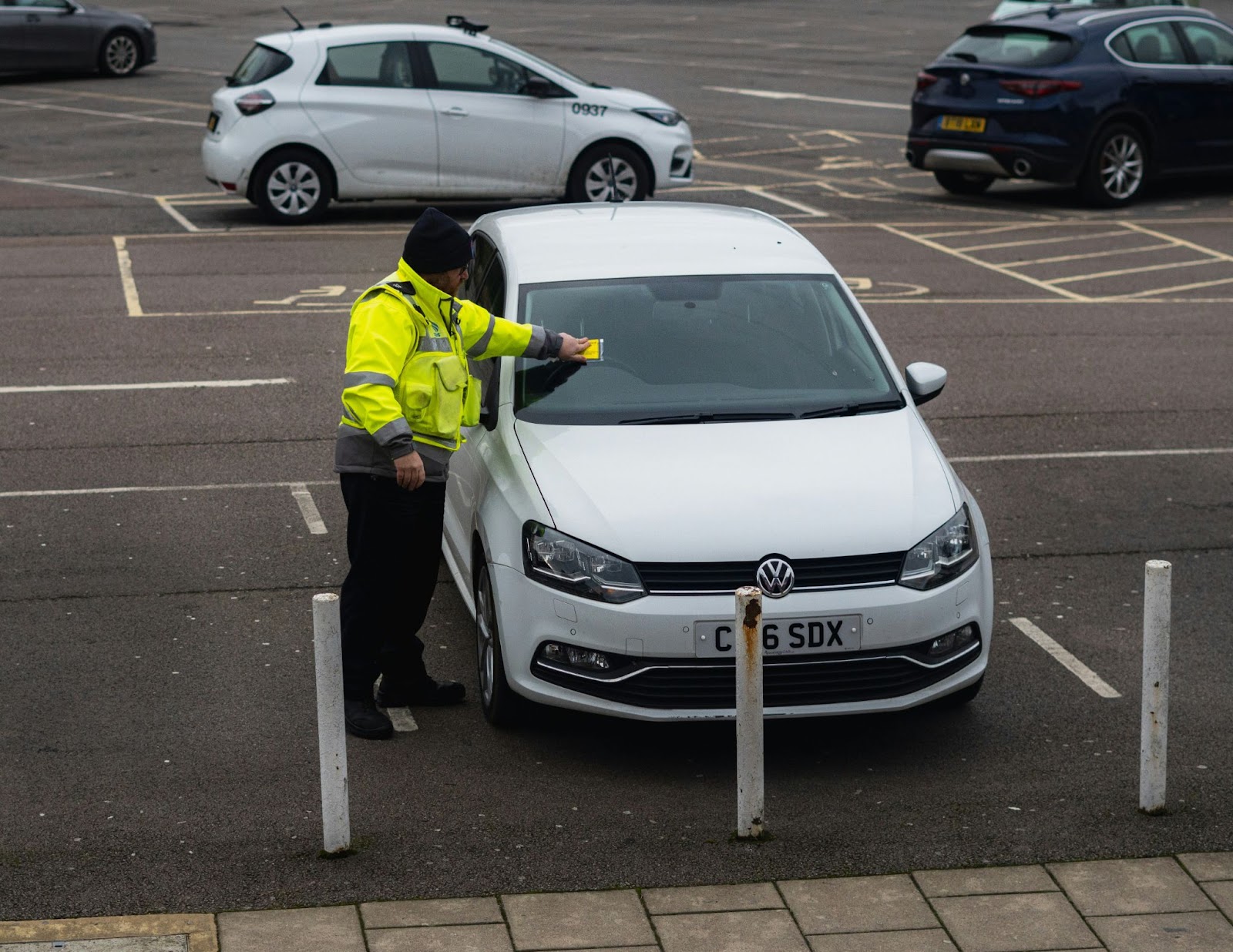 Parking officer placing a ticket on a white car's windshield in a parking lot