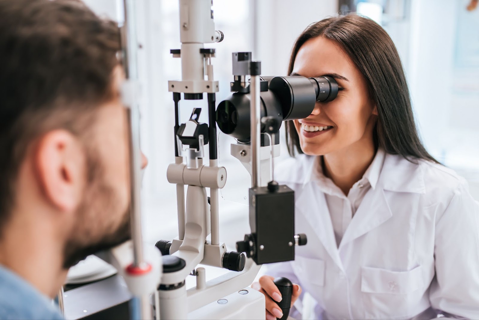 A female optometrist smiling while examining a male patient's eyes.