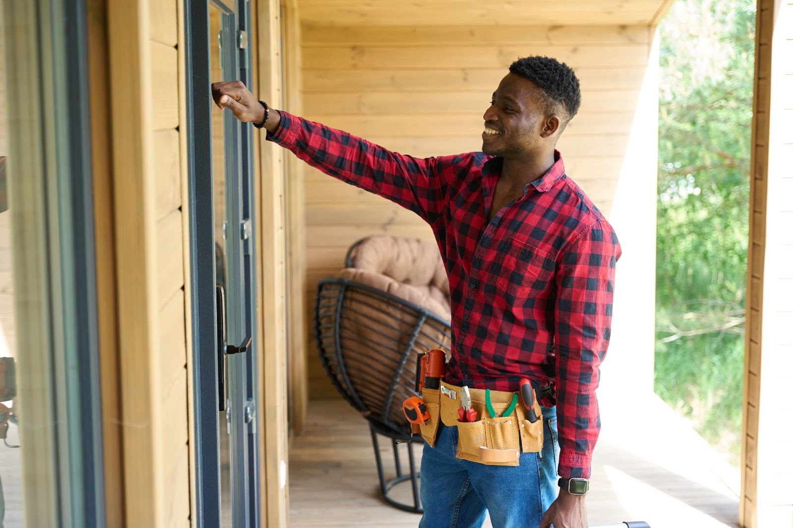 A smiling male contractor wearing a utility belt knocking on a door.