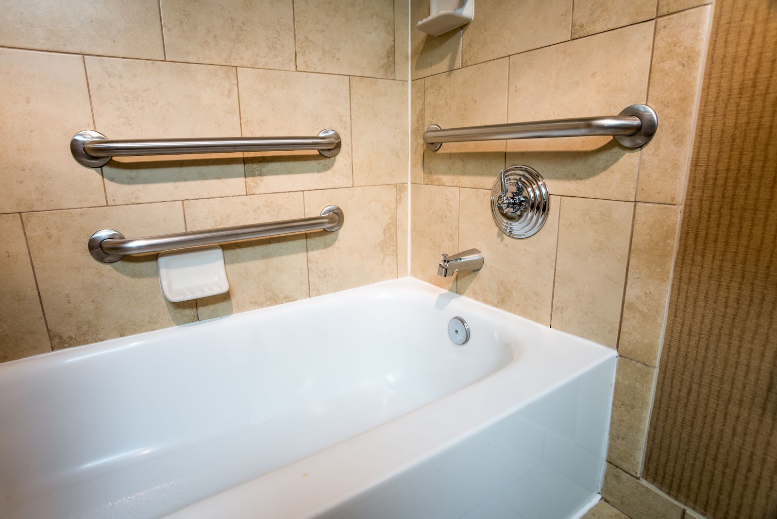 A tiled bathroom showcasing three grab bars for balance assistance over a porcelain bathtub