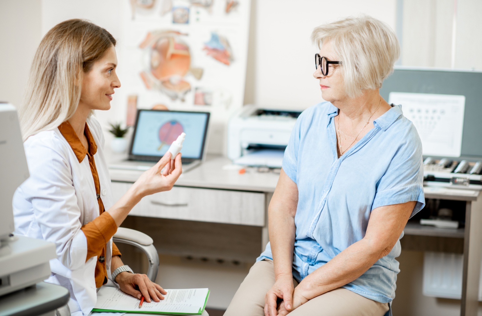 An eye doctor showing her patient a bottle of eye drops that can be used for dry eyes.