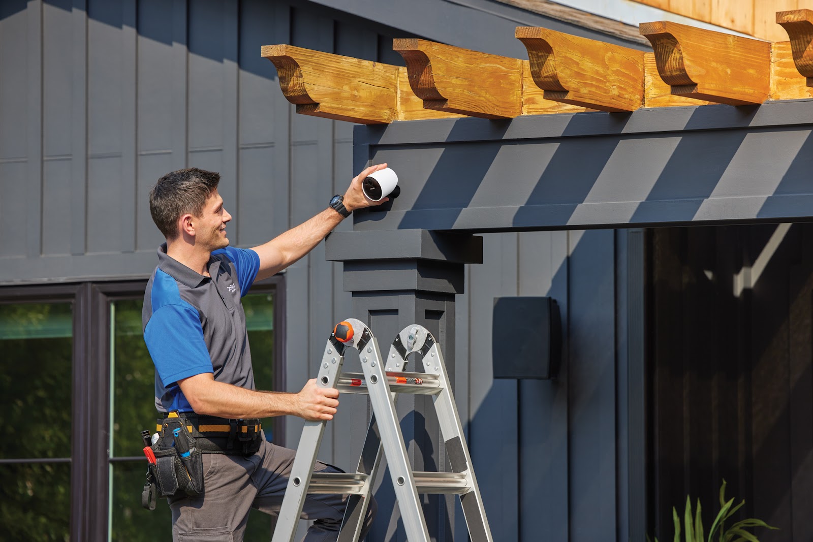 An OnTech employee standing on a ladder while installing the SimpliSafe® Outdoor Camera.