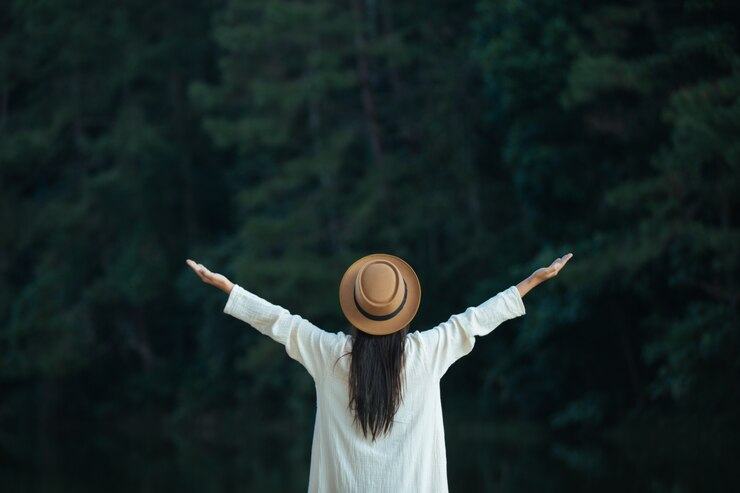 A woman with her back towards the camera wearing a brown hat and having her arms wide open