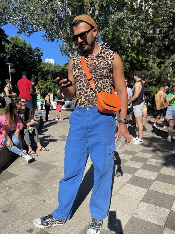 gay toronto gogo dancer and gay content creator Phil dressed in blue pants and tight leopard print tank top looking at his phone during gay toronto pride event at 519 community centre green space party