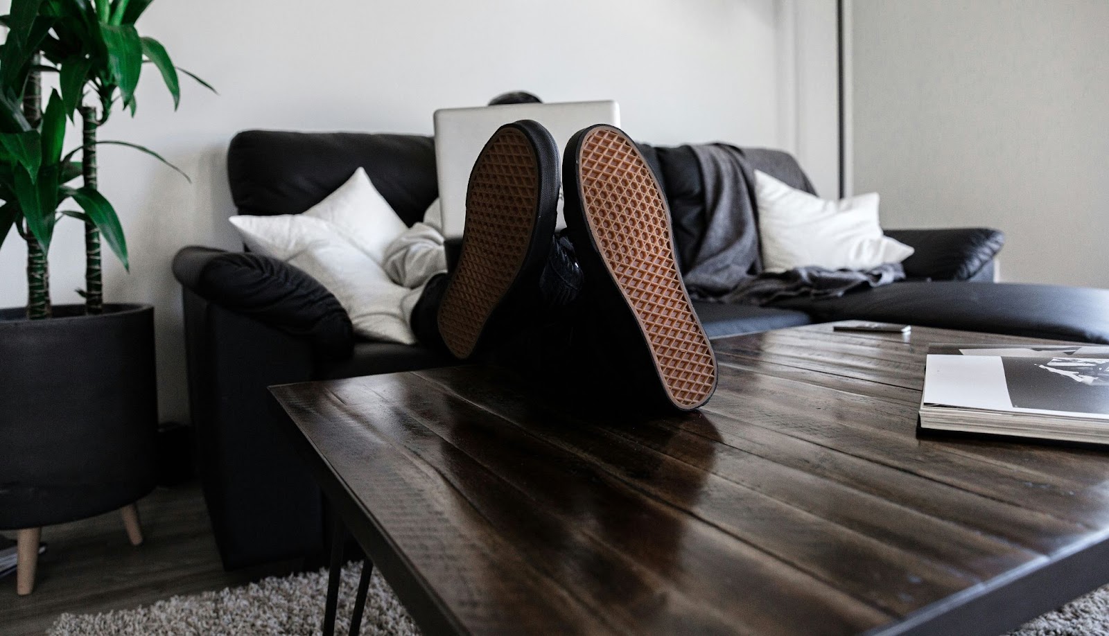 Person on sofa resting feet on coffee table while working on laptop