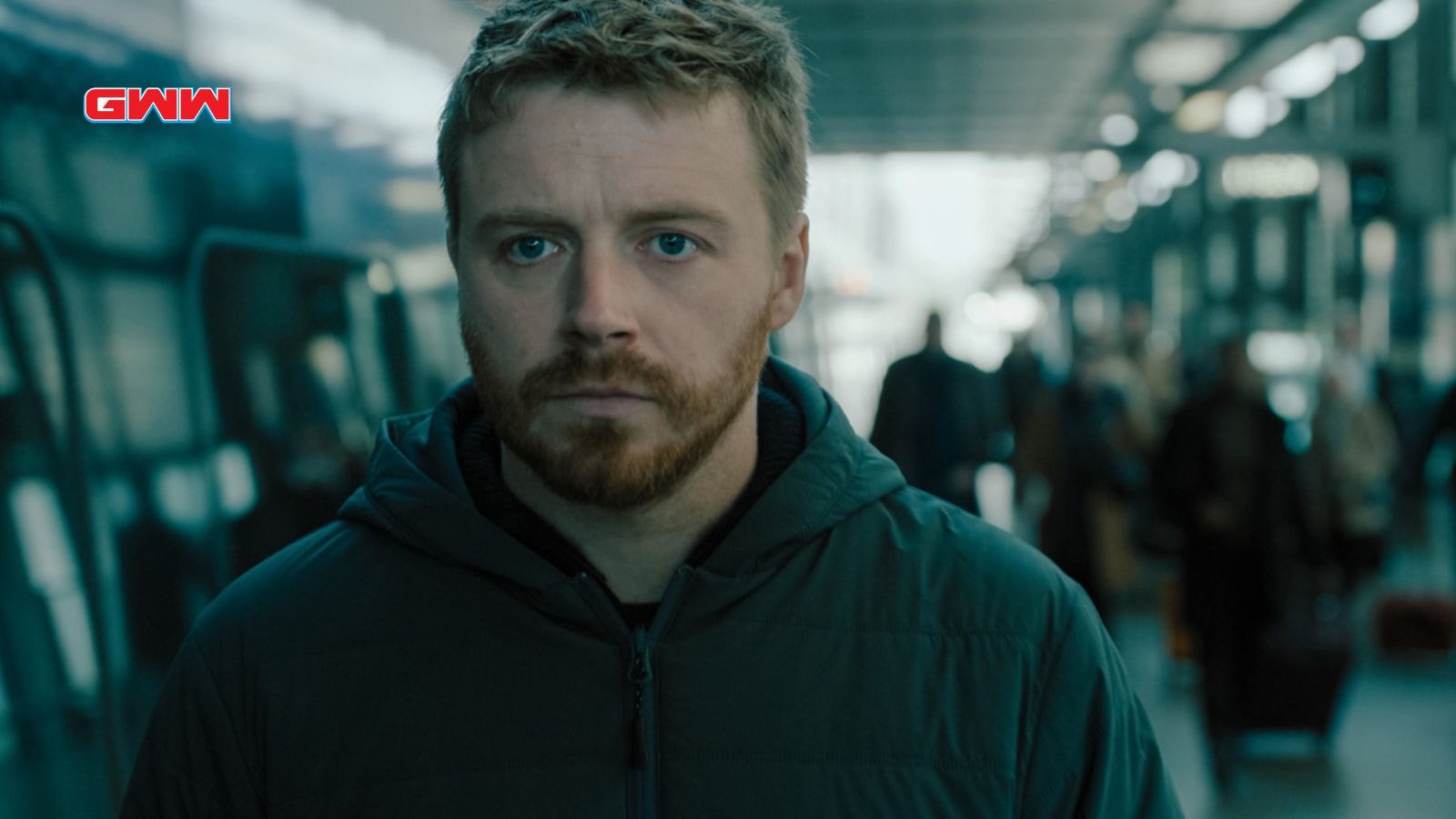 River in a crowded station, looking serious and pensive.