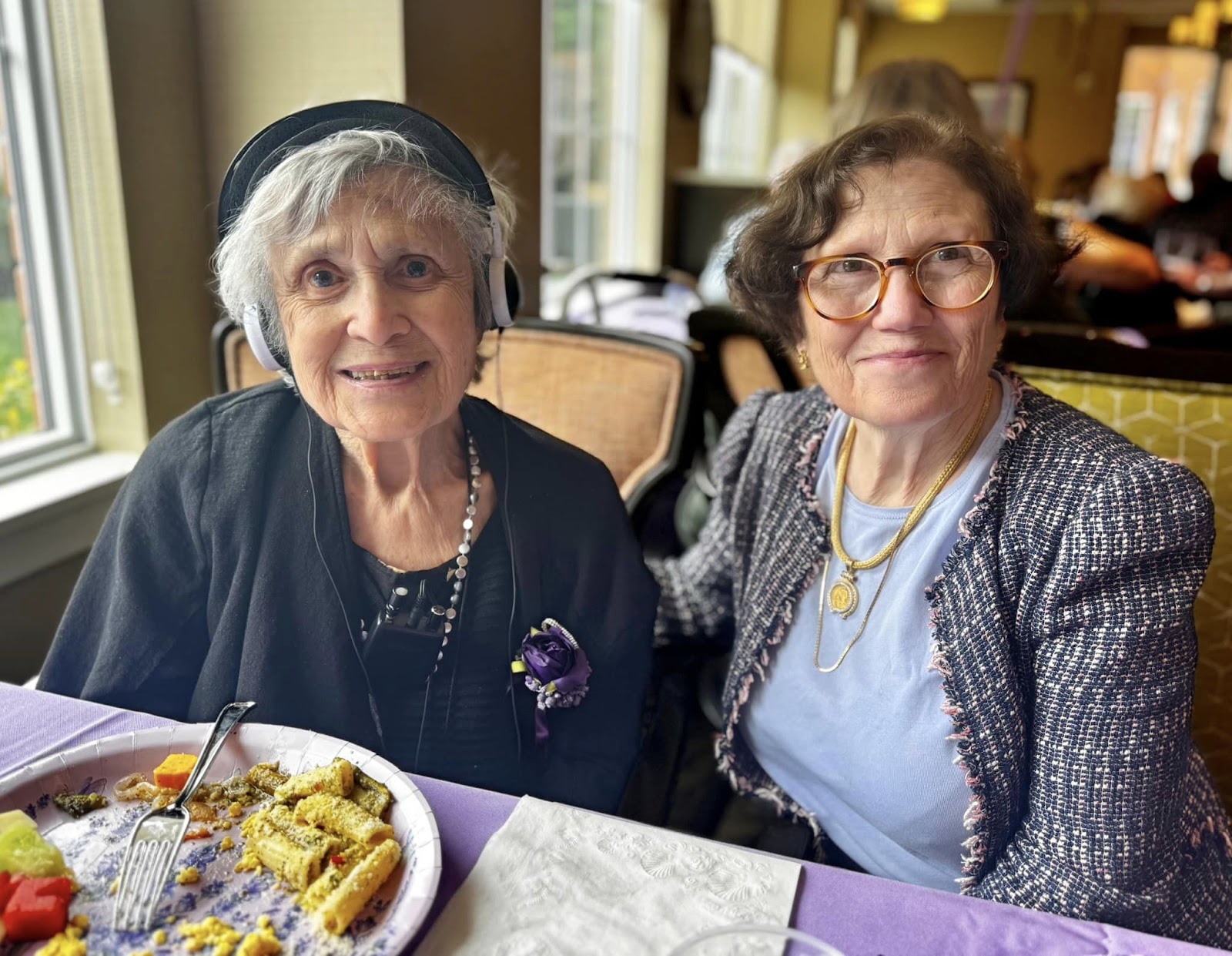 Two women smiling at the camera in an assisted living facility while sitting at a table