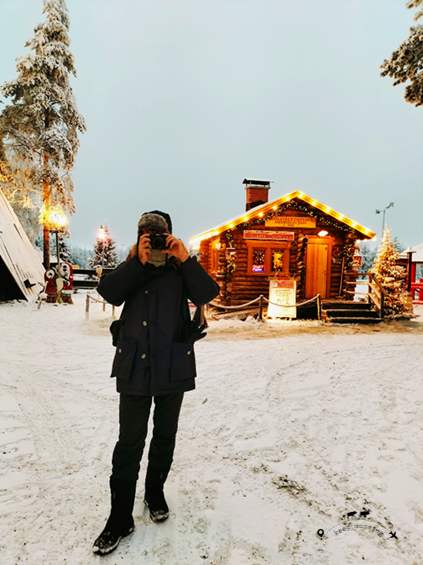 Tiziano taking a photo. In the background a typical wooden house with Christmas lights and a large tree on the left.