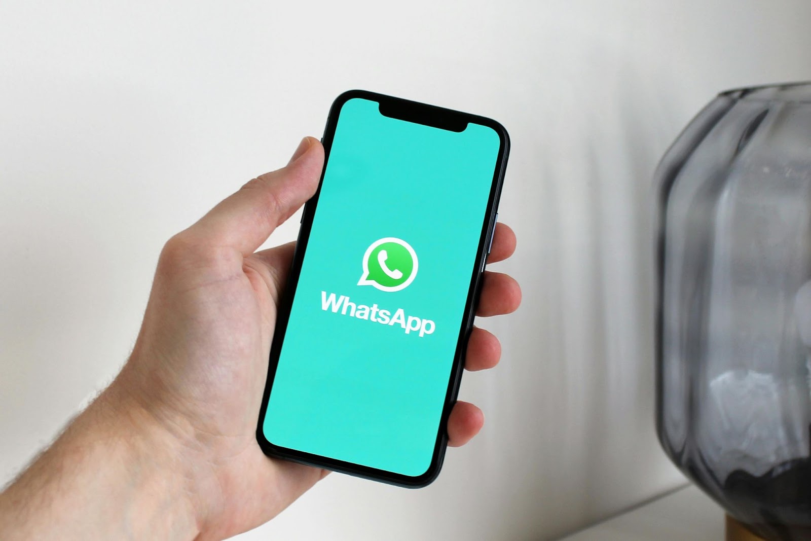 Hand holding a smartphone with the WhatsApp logo on the screen