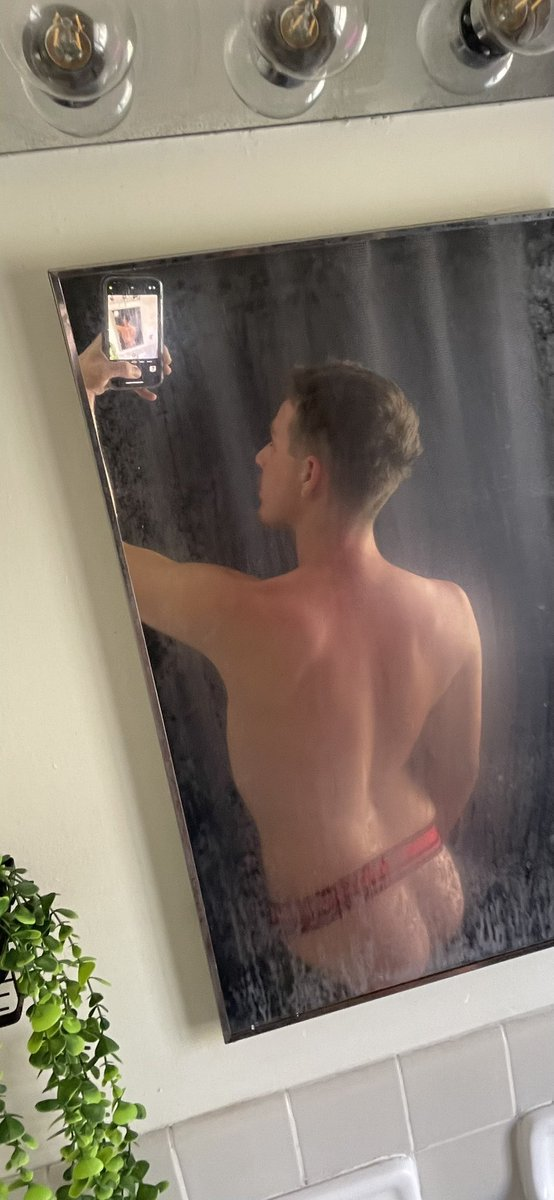 Dallas Knoxxx gay xxx onlyfans creator posing in a shower fogged mirror taking a selfie in a red and black jock strap showing off his twink butt