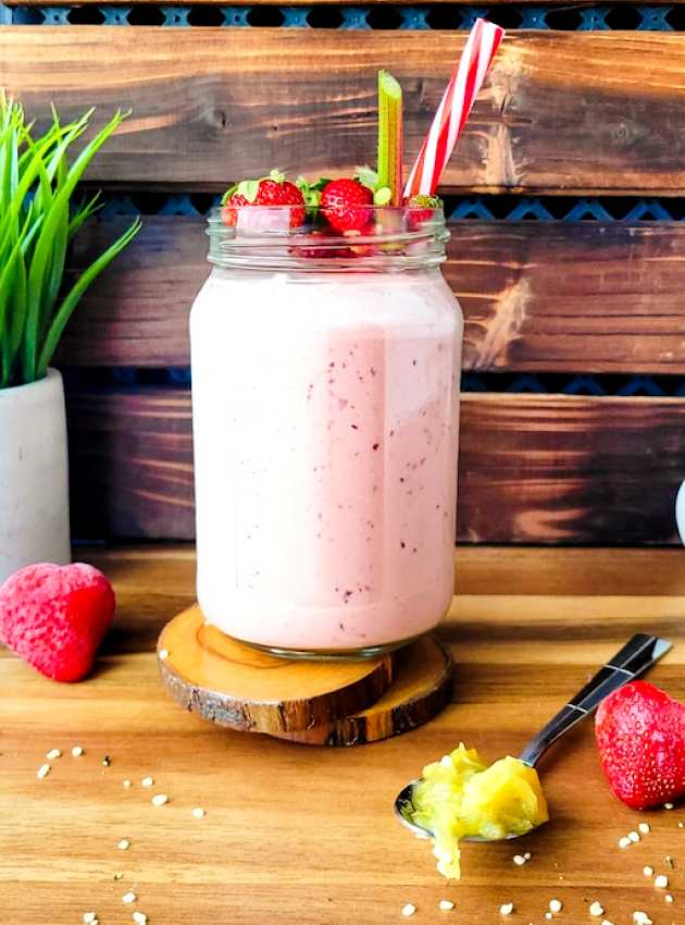 Pink strawberry and rhubarb protein smoothie in a glass, on a wooden board.