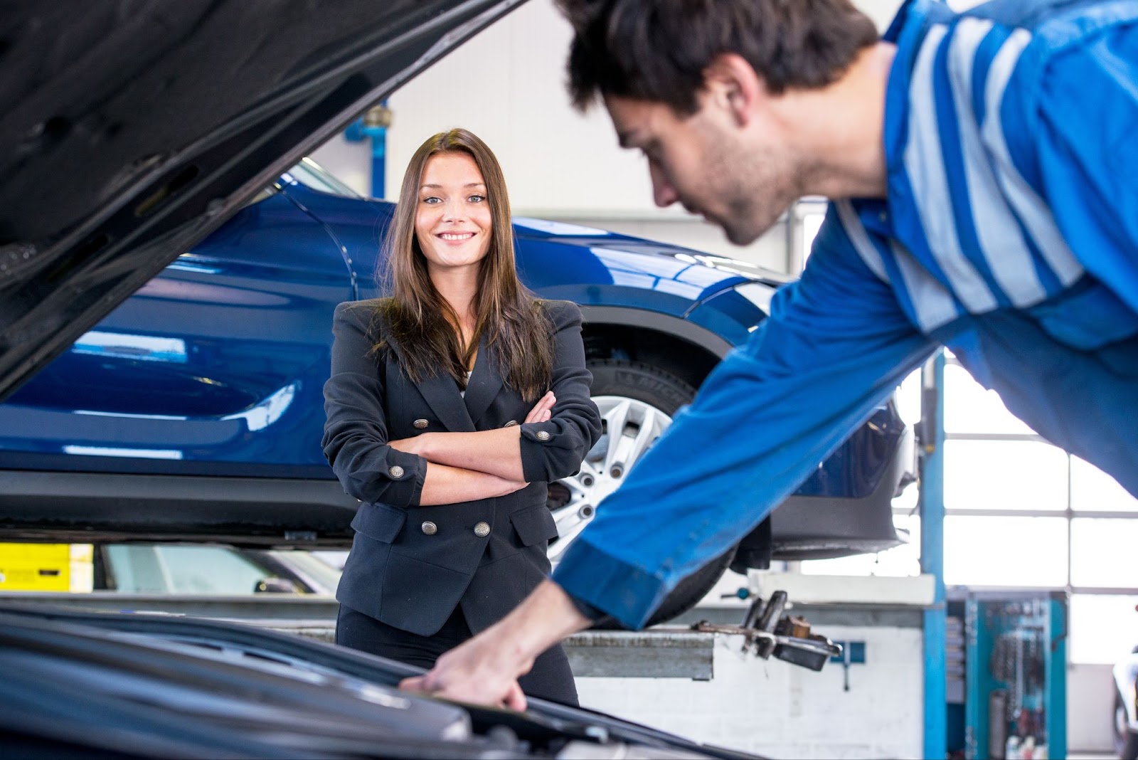 A young businesswoman smiling as a mechanic works on her radiator.