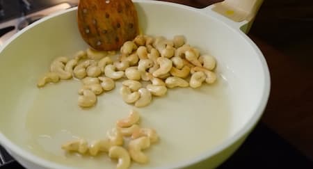Whole cashews frying in a pan until golden brown.