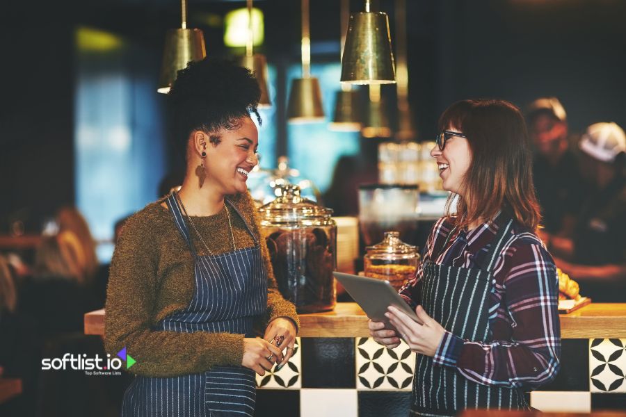 Two women in a café, one holding a tablet, both smiling.