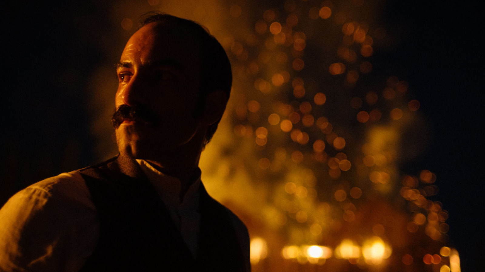 Gabriel Cañas en una escena nocturna como José Luis Echeñique, con un fondo de luces y fuego.