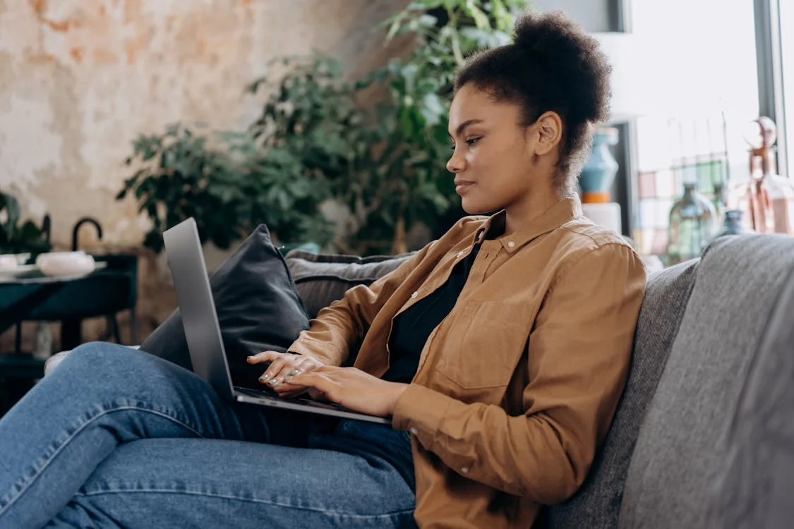 A woman sitting on a couch, doing work on a laptop