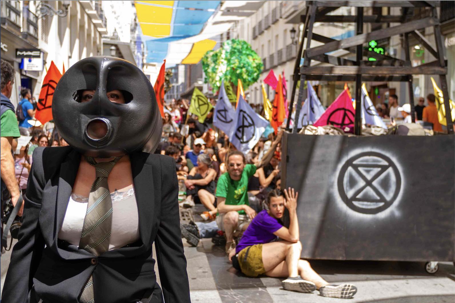 A rebel wears an oil drum mask leading a procession of colourful rebels.