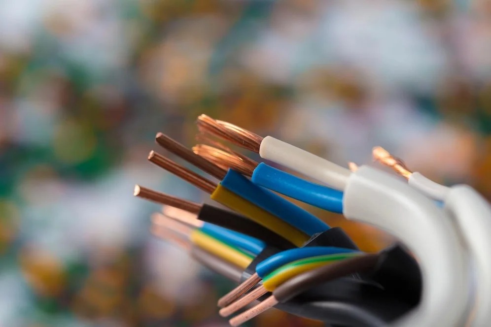 Close-up of a bundle of electrical wires with exposed copper ends against a blurred background.