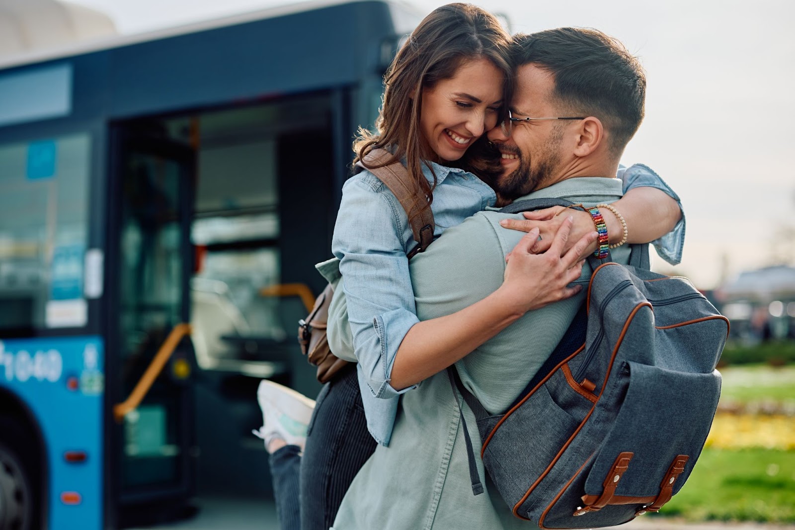 Casal sorridente abraçados em frente a um ônibus de viagens.