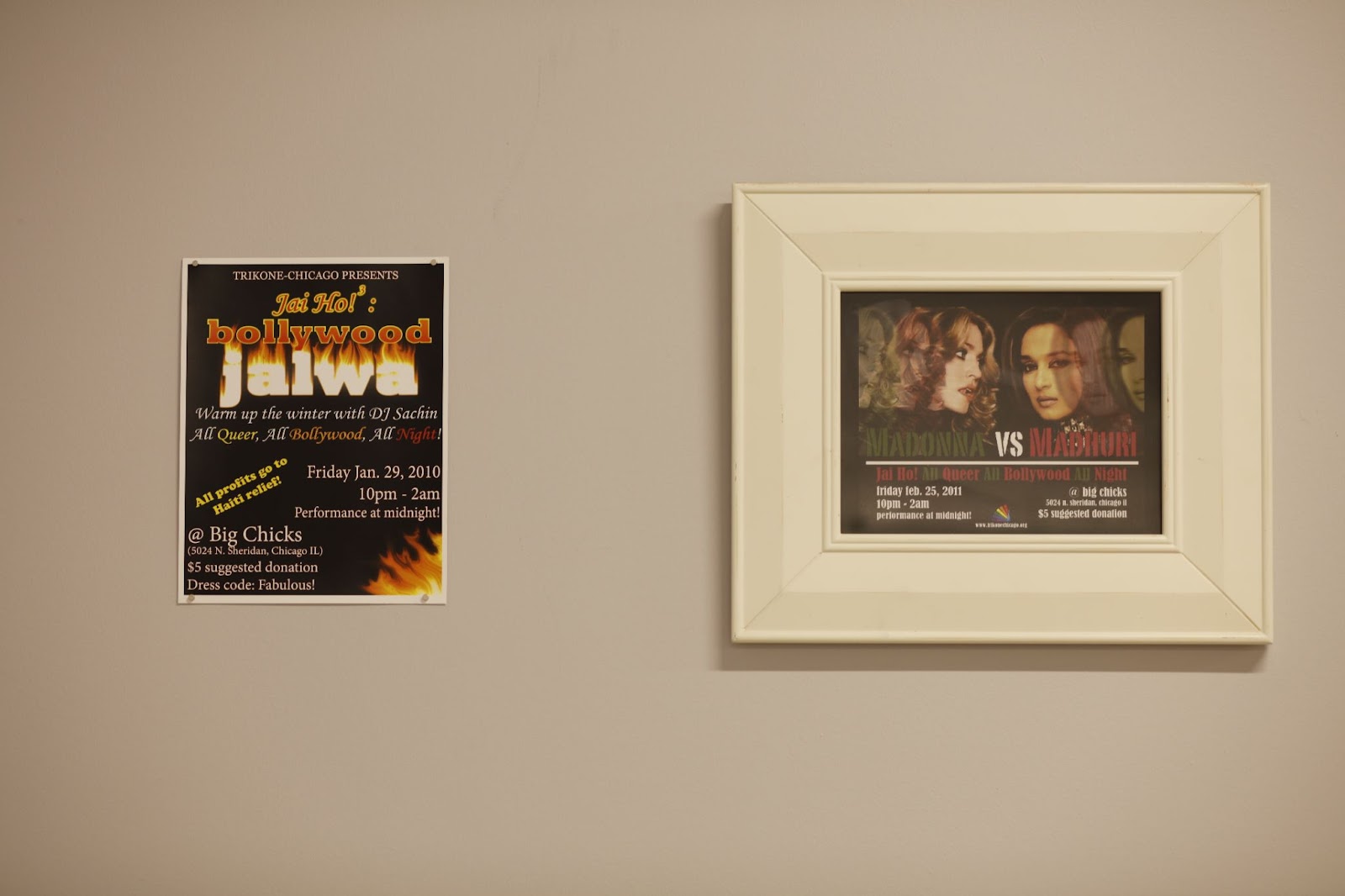 Image: Installation view, People Who Came Before Us. Two posters against a blank wall. The poster on the left is an unframed flyer for an event in 2010, Jai Ho! Bollywood Jalwa advertising queer Bollywood music all night, where the proceeds go to providing relief in Haiti. On the right, in a thick white frame, is a flyer for Madonna vs. Madhuri event hosted as part of the same series in 2011.