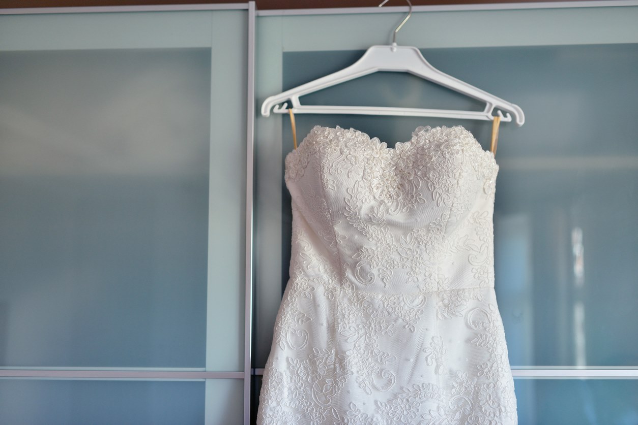 A white wedding dress hanging on a door indoors.