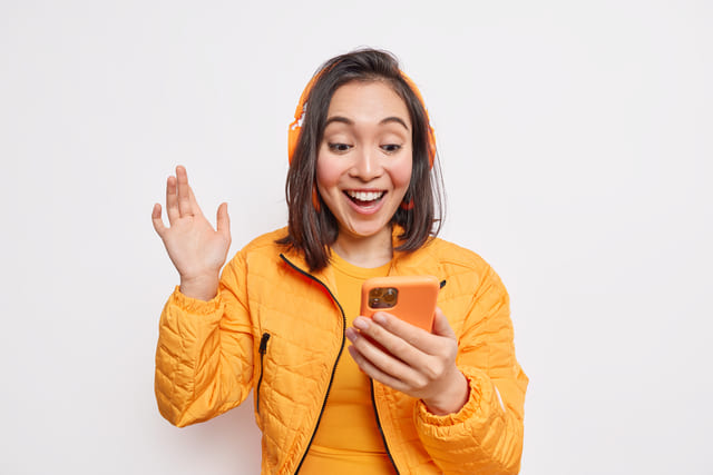 A person wearing orange jacket and headphones holding a phone  Description automatically generated