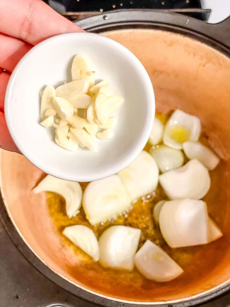 a small bowl of garlic being held above a pot with onions.