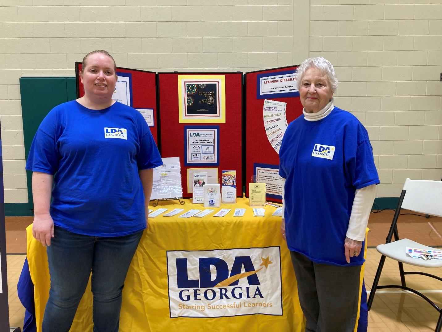 Two women standing next to a table

Description automatically generated