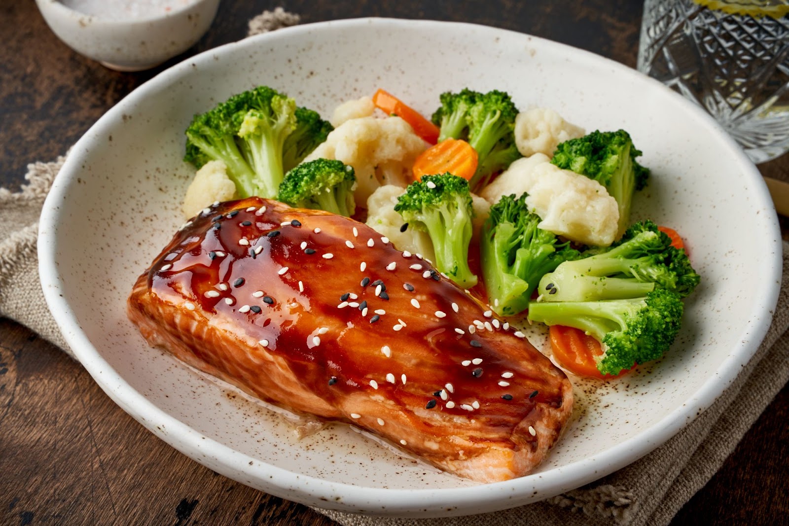 A plate of salmon and crunchy broccoli, carrots, and cauliflower.