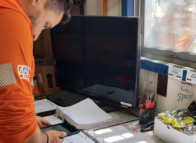 an using a cell phone next to a computer monitor and binders. 