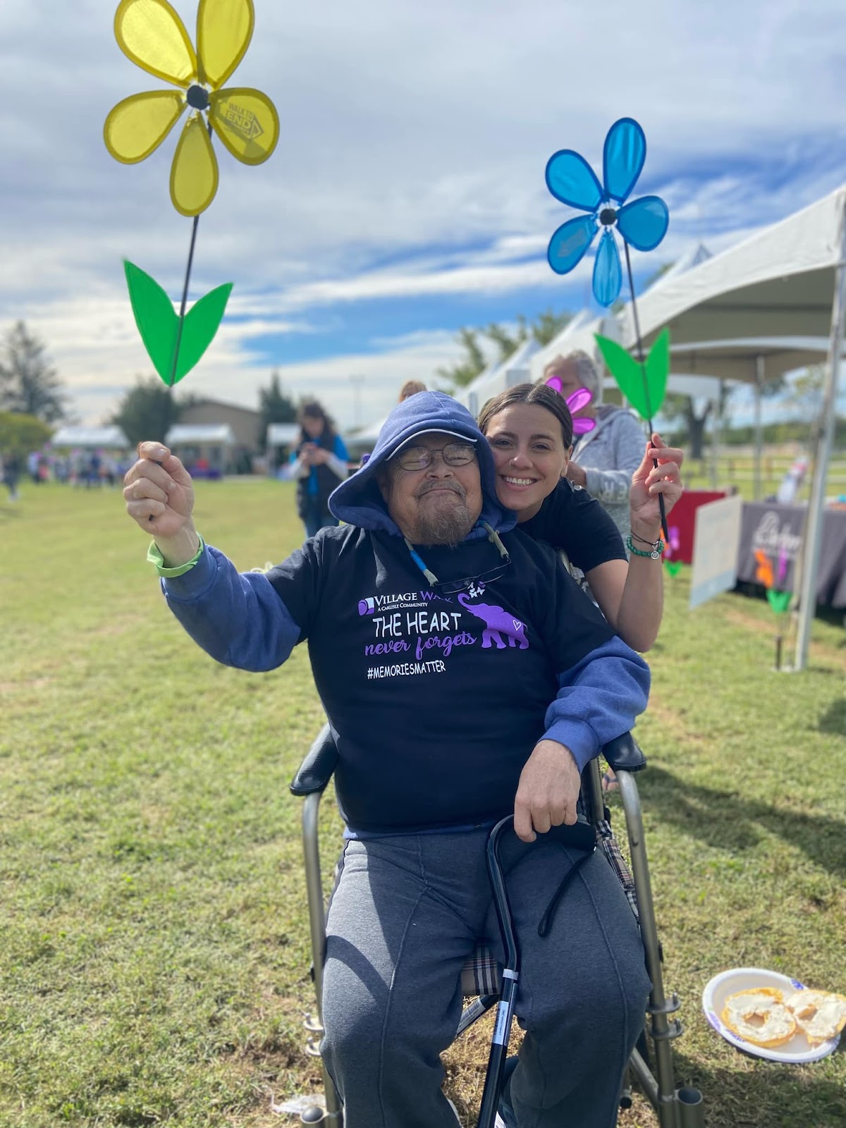 A senior citizen and an aide holding flower props and smiling at the camera