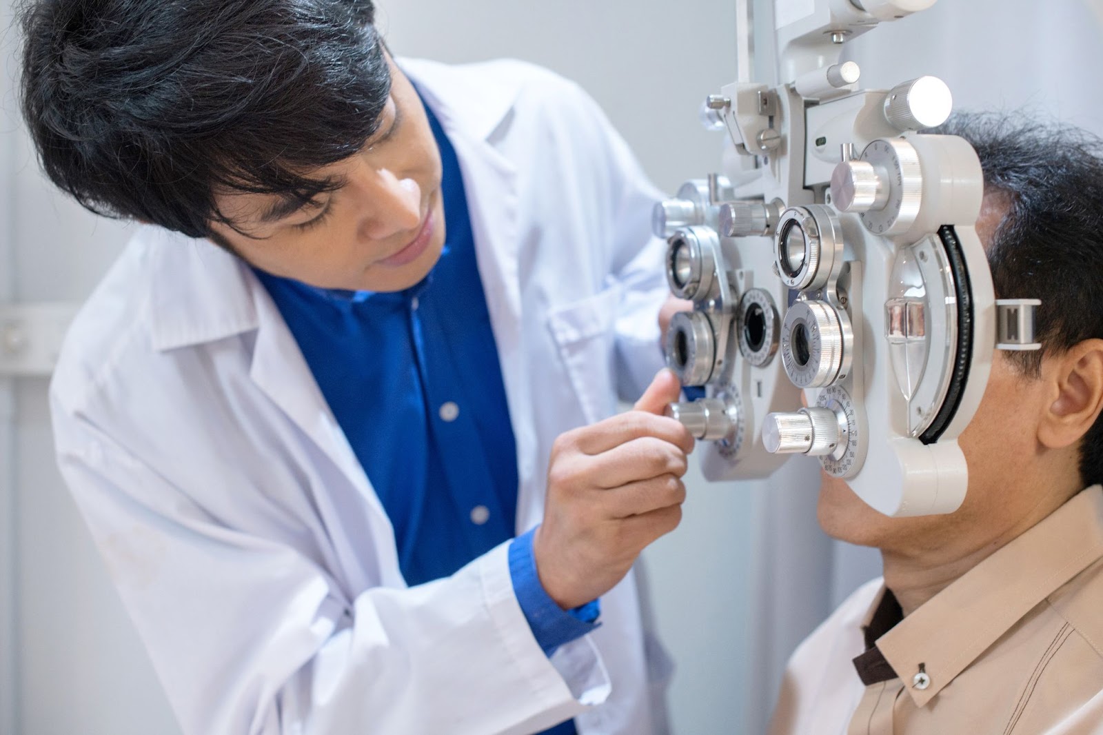 An optometrist adjusts the phoropter to find the correct lens power for their patient while the patient sits in the exam chair.