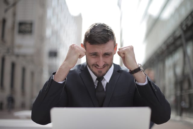 Businessman in suit and tie appears overwhelmed, holding head in hands while gazing at laptop.