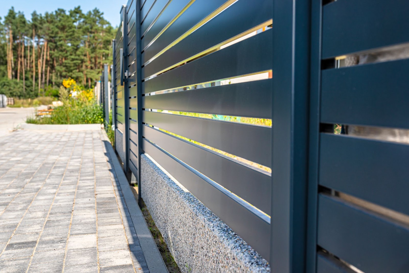 Modern black gates are securing a home. In the background is a forest.