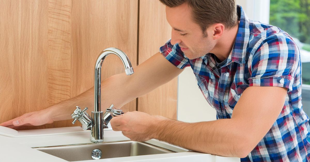 A man in a blue shirt fixing a kitchen sink with a wrench.