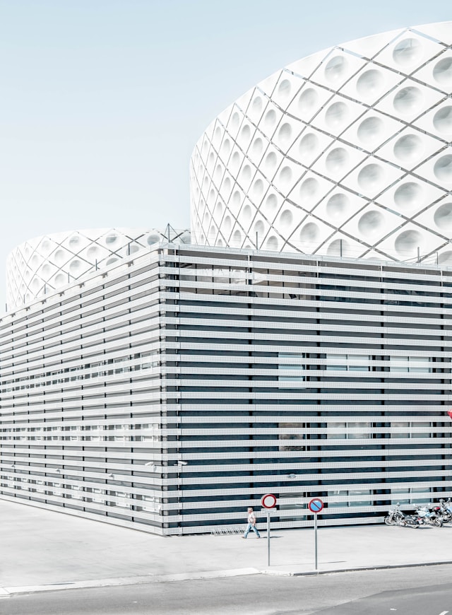 A white louvered building facade with a curved white perforated facade behind designed using parametric design principles