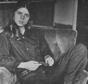 A female student at Amherst wearing jeans and a button-up shirt lounges on a sofa chair.