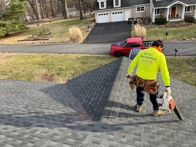 Boundless Roofing & Chimney roofer, equipped with tools, doing roof repairs on the roof of a residential house.