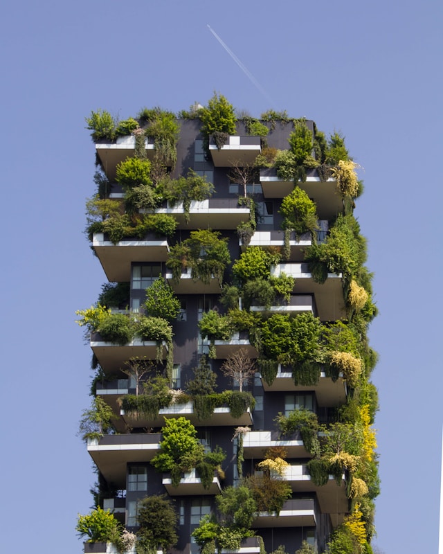 A tall glass building with projections filled with plants and a clear sky in the background