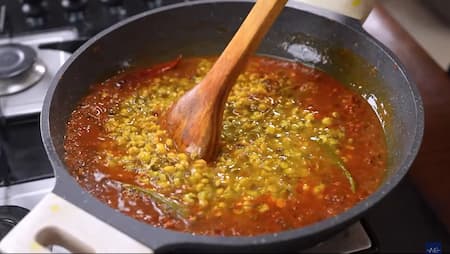 Boiled dal being added to the masala base in a pan, combining both to create the rich dal mixture.