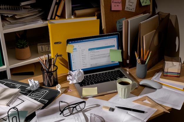 View of office desk with messy workspace and laptop