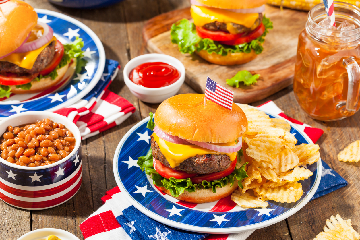 A close-up of a hamburger and sides with an American flag on a toothpick stuck on top of the bun.