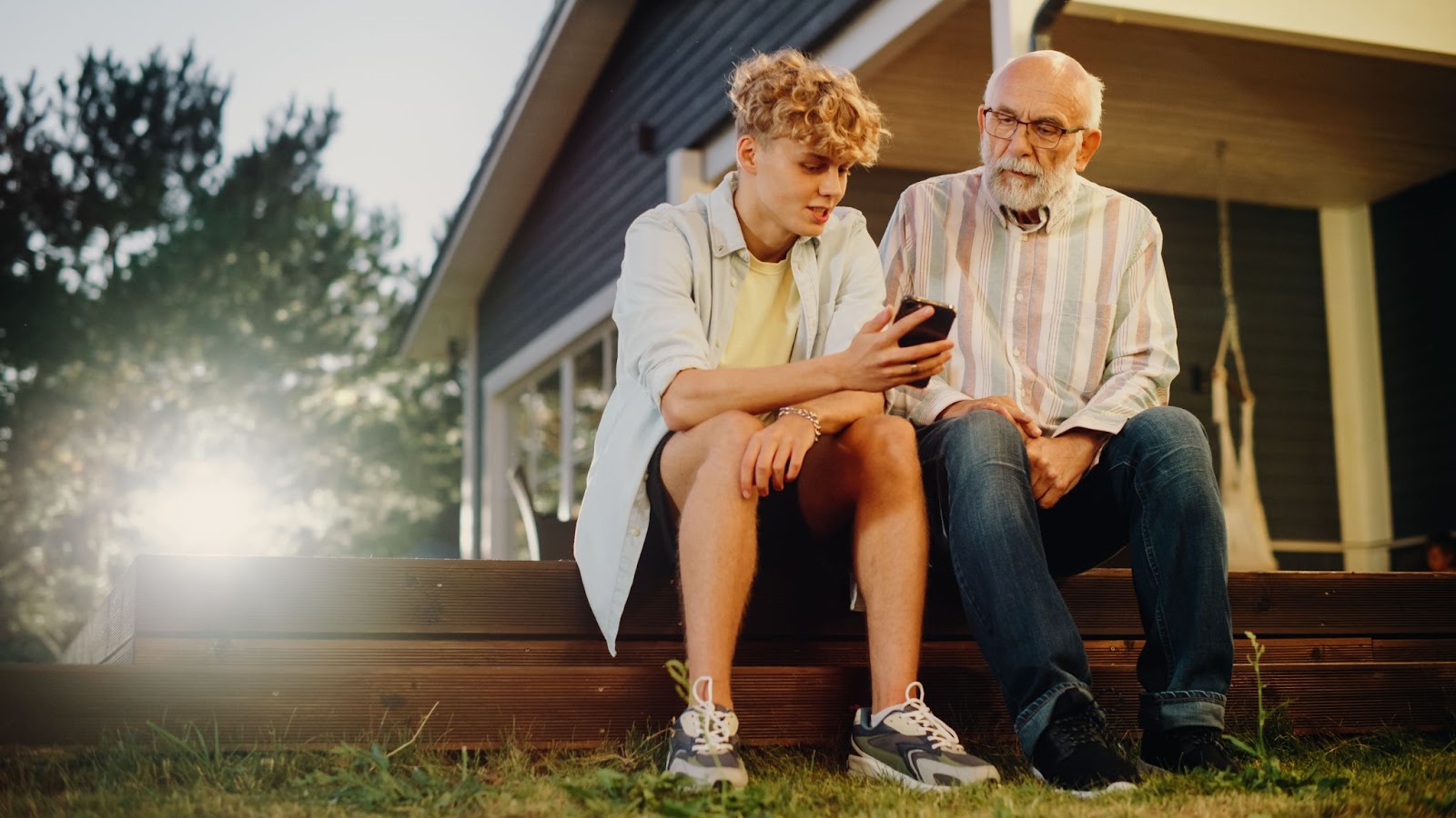 A grandson sitting outside with his grandfather telling him a story & showing him something on his cellphone