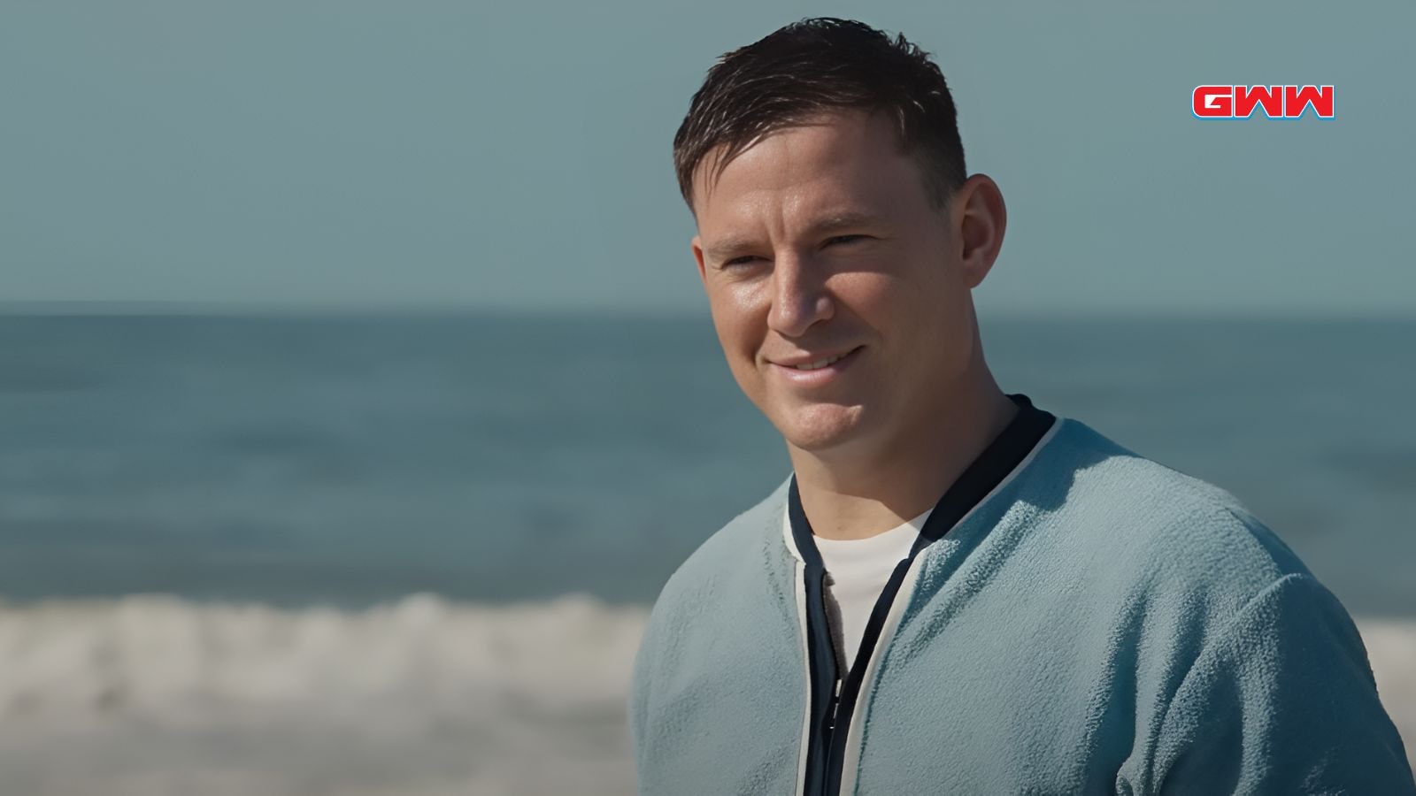 Cole con chaqueta azul sonriendo en la playa con fondo marino.