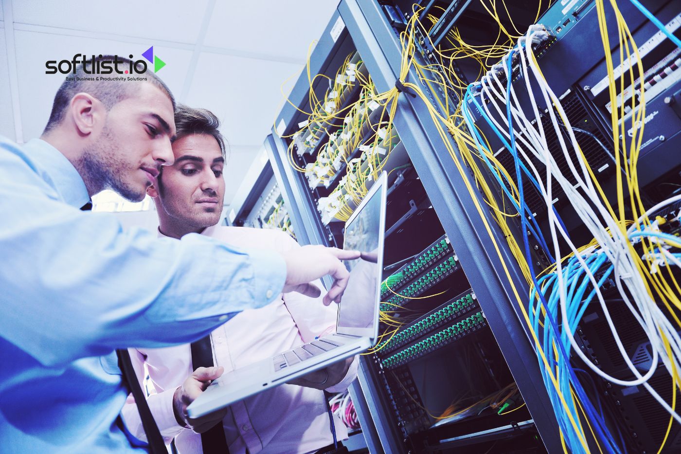 Two IT professionals discussing while working on a laptop in a server room